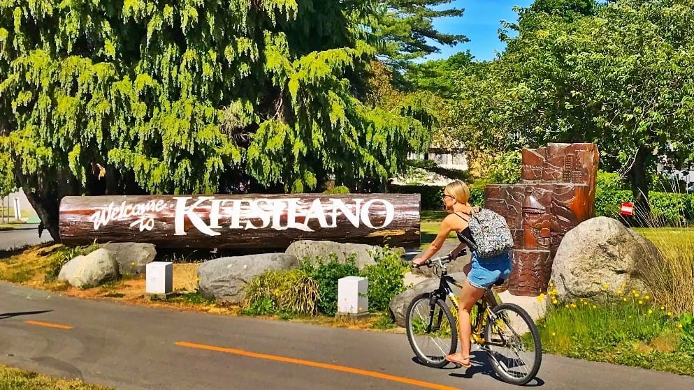 A girl biking pass by Welcome to Vancouver Kitsilano Sign